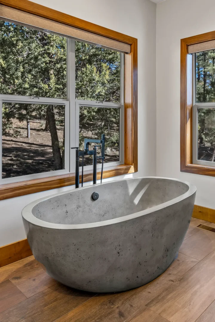 reestanding concrete soaking tub with black floor-mount faucet and panoramic forest views in Flagstaff AZ bathroom remodel by Barden Home Builders