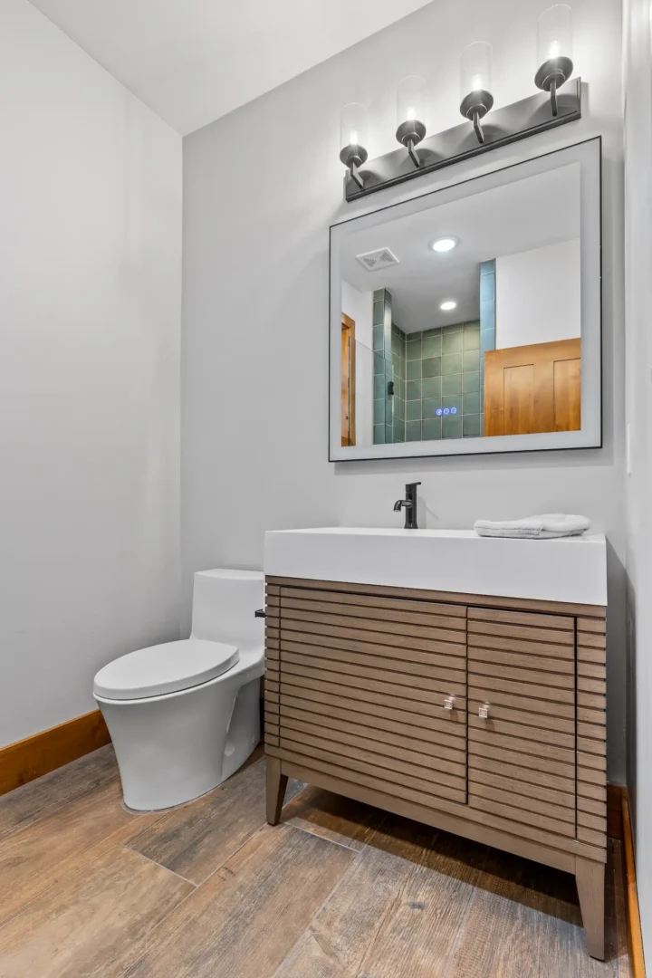 Guest bathroom remodel in Flagstaff AZ with wood-slat vanity, vessel sink, black matte faucet, and lighted mirror by Barden Home Builders