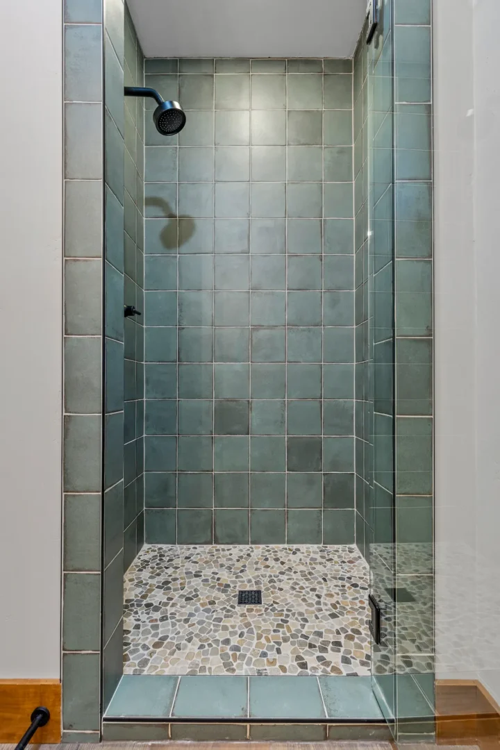 Flagstaff bathroom remodel shower with custom teal square tile surround, pebble mosaic floor, and black fixtures by Barden Home Builders
